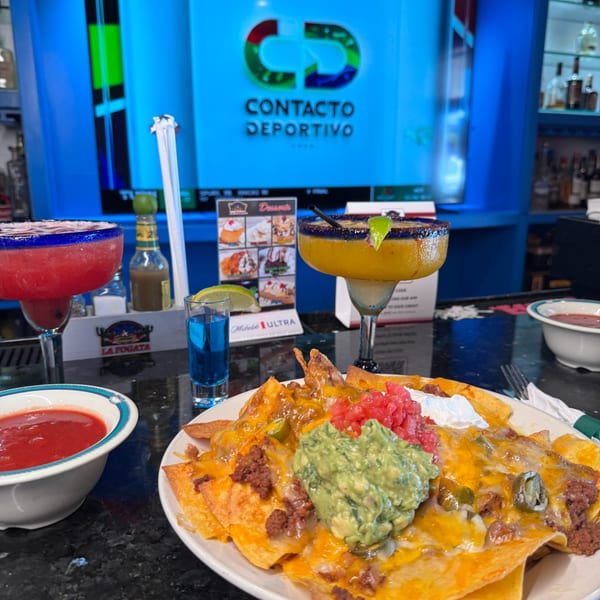 Nachos with guacamole, sour cream, and salsa, alongside two margaritas and a blue shot.